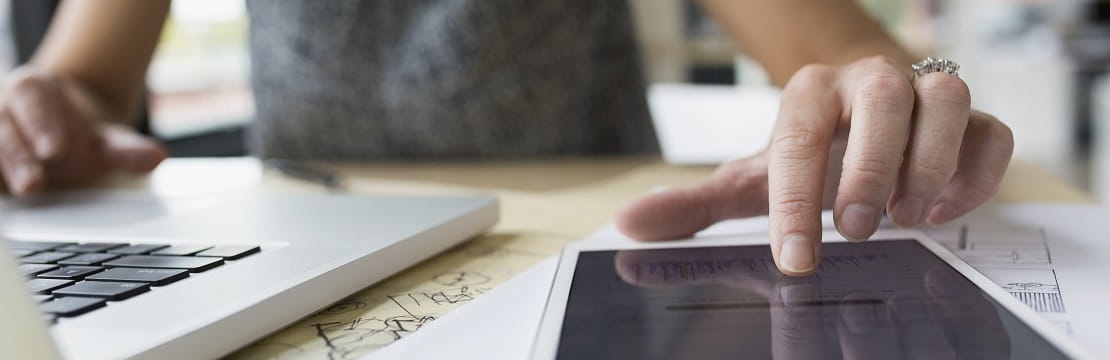 Woman working simultaneously on a laptop and tablet at a desk. 