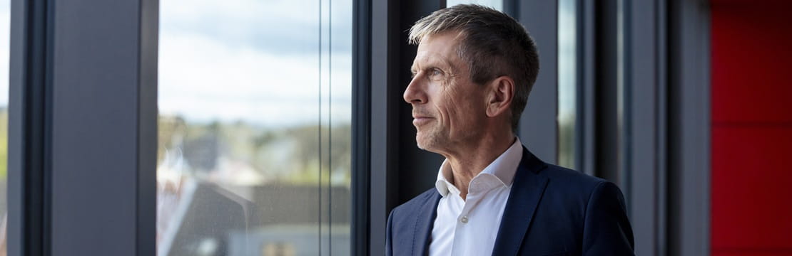 Corporate executive looking out an office window, reflecting on retirement planning and long-term financial strategy.